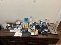 Wide view of assorted optical lenses and microscope parts on table including boxed items and various metal instruments.