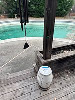 Wood deck near pool with ceramic garden stool on deck and metal wind chime hanging from wooden post