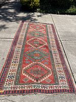 Full view of lengthwise runner rug laid flat on driveway, showing five central diamond medallions and border design