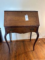 Front view of antique secretary drop front desk showing curved legs, scalloped apron, and wood grain.