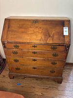 Front view of the closed secretary desk showing 4 drawers and wood finish with metal handles.