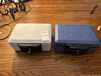Two portable safes side by side on wooden surface, one gray and one blue, showing general condition and size
