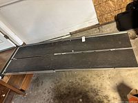 Full view of the folded aluminum wheelchair ramp with dark non-slip surface, showing fold line in middle.