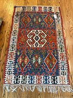 Full view of the woven rug laid flat on wood floor showing overall geometric pattern and fringed edge.