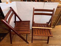 Pair of wooden folding chairs, one folded flat and one open showing slatted seat and backrest, dark stain finish