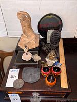 Front and angled view of lot showing multiple figures, cast iron rest, pottery plate, napkin rings, brass weight, and other items with ruler for scale.