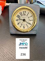 Front view of Tiffany & Co quartz alarm desk clock showing white dial, Arabic numerals, and brass bezel within a blue leather case.