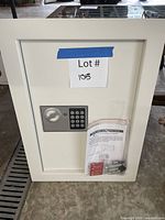 Front view of white electronic wall safe with keypad and accessories bag attached