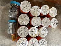 Group of orange canisters with white lids labeled with bolt sizes alongside two clear jars of hardware