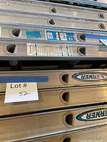 Stack of aluminum ladders, blue Werner logos, Lot 52 tag indicates subject ladder