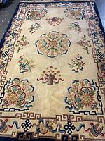 Photo showing overall rectangular handmade wool rug with a cream background and floral and geometric decorations.