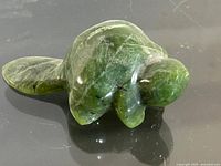 Green marble beaver figurine showing front and side profile on reflective surface.