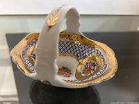 Angle view of Limoges porcelain basket showing floral paintings, gold gilding, and blue lattice design inside.