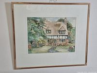 Full view of framed watercolour painting of cottage in natural setting.
