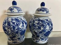 Pair of blue and white Chinese porcelain ginger jars with lids showing floral and vine pattern motifs on all sides.