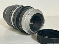 Close-up photo of the rear mount of the Tonika Tele Auto 135mm camera lens showing aperture lever and lens mount details, with rear lens cap removed and placed beside the lens.