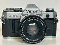 Front view of the Canon AE-1 camera with attached Canon FD 50mm f/1.8 lens showing model name and lens details.