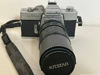 Front view of Minolta SR-T 102 camera showing metal top, black body, lens cap with KitStar branding and camera strap attached.