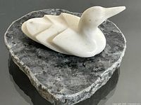 White granite loon carving displayed on a rough black granite base, showing side profile and polished finish.