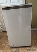 Full front view of white GoldStar bar fridge with smooth door and gray handle trim.