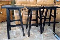 Three black wooden stools arranged side by side showing differences in wear level.