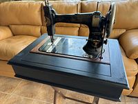 Side view of the black vintage White brand treadle sewing machine mounted on a black wooden cabinet with storage inside.
