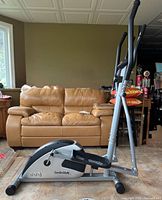 CardioStyle elliptical machine side view showing seat and foot pedals, with visible floor tiles and surrounding furniture.