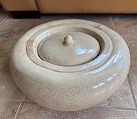 Front-angle view of round beige crackle glazed ceramic fire pot with lid on and smooth glossy finish.