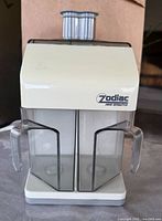 Front view of Zodiac juice extractor showing cream colored body and two clear containers with handles for collecting juice and pulp.