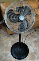 Front view of the large black floor standing fan showing metal cage, black blades, and round base.