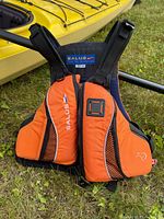 Front view of the orange and black Salus kayak life jacket hanging with kayak in background.