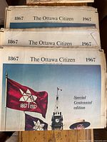 Photo showing three copies of The Ottawa Citizen Centennial edition from 1867-1967 with front page featuring Canadian Centennial flags and a Mountie.
