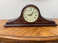 Front view of the antique composite mantel clock with Roman numerals on the clock face, sitting on a wooden table.
