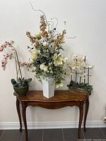 Full view of three floral arrangements in various vases placed on wooden console table against white wall