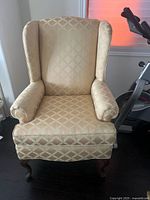 Front view of beige/gold diamond patterned wingback armchair showing the full upholstery and wooden legs.