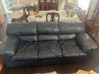 Front view of the dark blue leather 3-seater sofa showing three seat cushions and wide padded armrests, highlighting the leather material and signs of use.