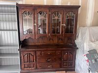 Front view of a pine wooden dining room cabinet showing four glass-panel doors on top and four wooden doors with three drawers below. Visible wear and tear consistent with used condition.
