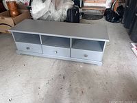 Grey IKEA TV stand with three open shelves and three drawers with metal knobs, showing minor chips and used condition.
