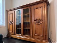 Full frontal view of oak veneer wall cabinet with two central glass paneled doors showcasing shelves inside and solid wood doors on either side with carved decorative details.