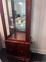 Front view of antique display cabinet showing glass doors and wooden lower storage doors with decorative metal handles.