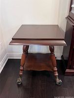Square wooden end table with turned carved legs and brass caster wheels, dark finish, scalloped bottom shelf edge.