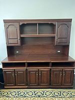 Photo of a dark brown wooden credenza with two upper cabinets, two open center shelves, a broad countertop, and four lower cabinets.
