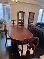 Photo of rectangular solid wood dining table with extension leaf, seats 6, surrounded by four matching wooden chairs with light upholstery.