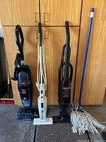 Three stick vacuums and mop standing upright