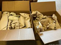 Two open cardboard boxes containing wrapped frog figurines