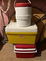 Stack of four coolers: white/red jug, yellow Coleman cooler, two red coolers