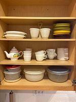 Cupboard shelves showing teapot, Pyrex and Corelle cups, dip bowls, ovenware pots, Tupperware bowls and lids