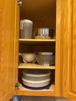 Cabinet shelf showing pitcher, mixing bowl, colander, mesh strainer and stacked plastic containers