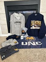 All items in lot laid out showing sweatshirts, three polo shirts, beanie, cowbell, flag, blanket