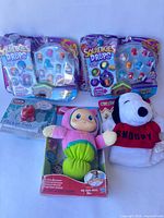 Group shot of all items including three Squinkies packs, Flicker Fish, Gloworm plush, Snoopy plush